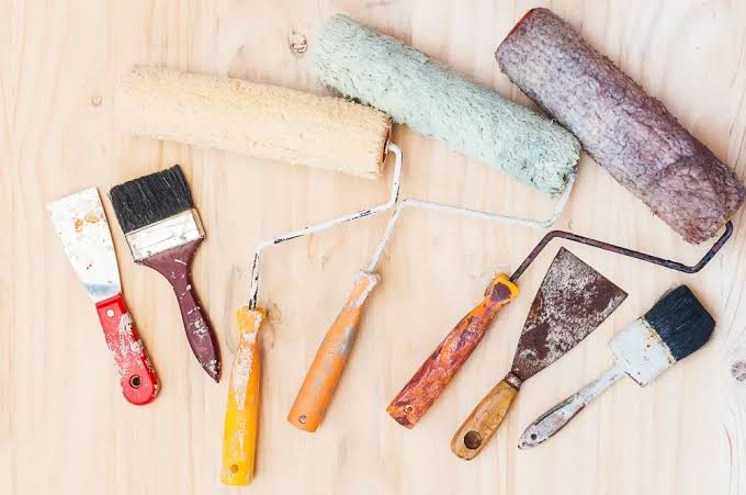 Paint rollers, brushes and scrapers laid out on a wooden surface