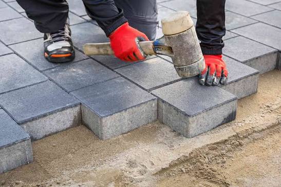 Paver tapping a concrete block into place with a mallet