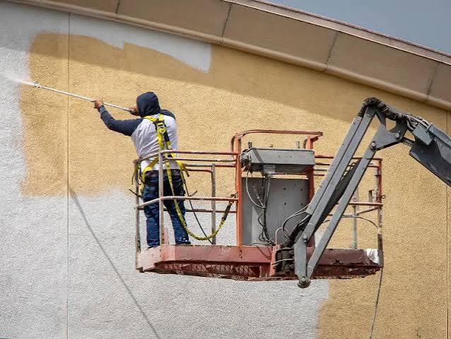 Painter spraying a large exterior wall from a cherry picker