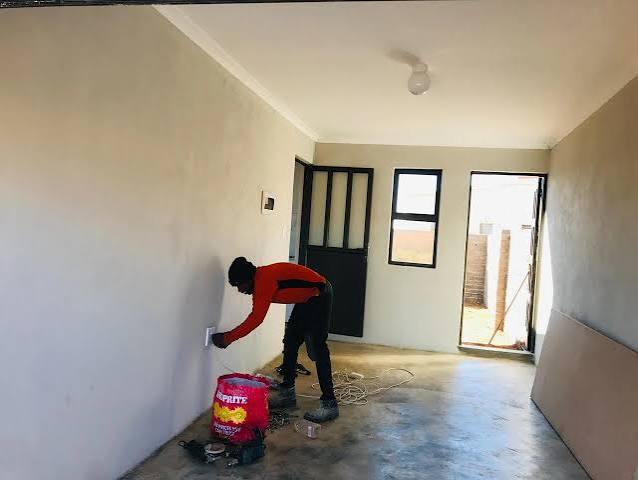 Painter cutting in around a wall socket in an empty room
